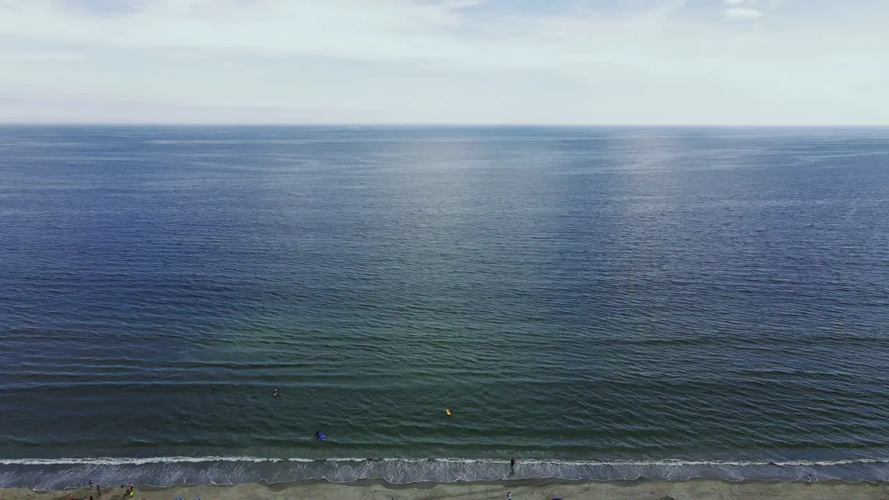 Aerial high footage of vast ocean scene sun rays being reflected on the water surfers and swimmers at bottom of frame