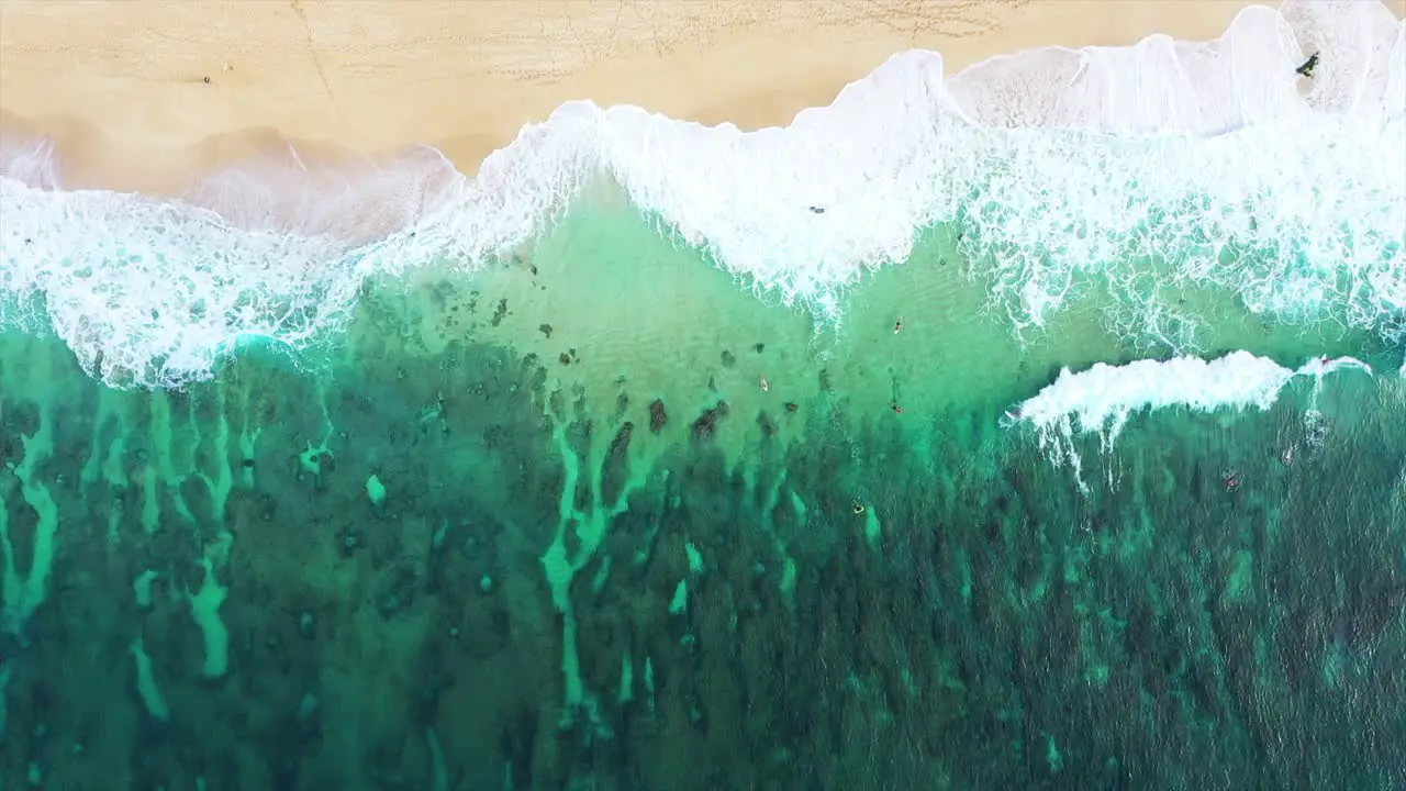 Aerial Surfers far below paddle over reef out to sea Hawaii North Shore beach