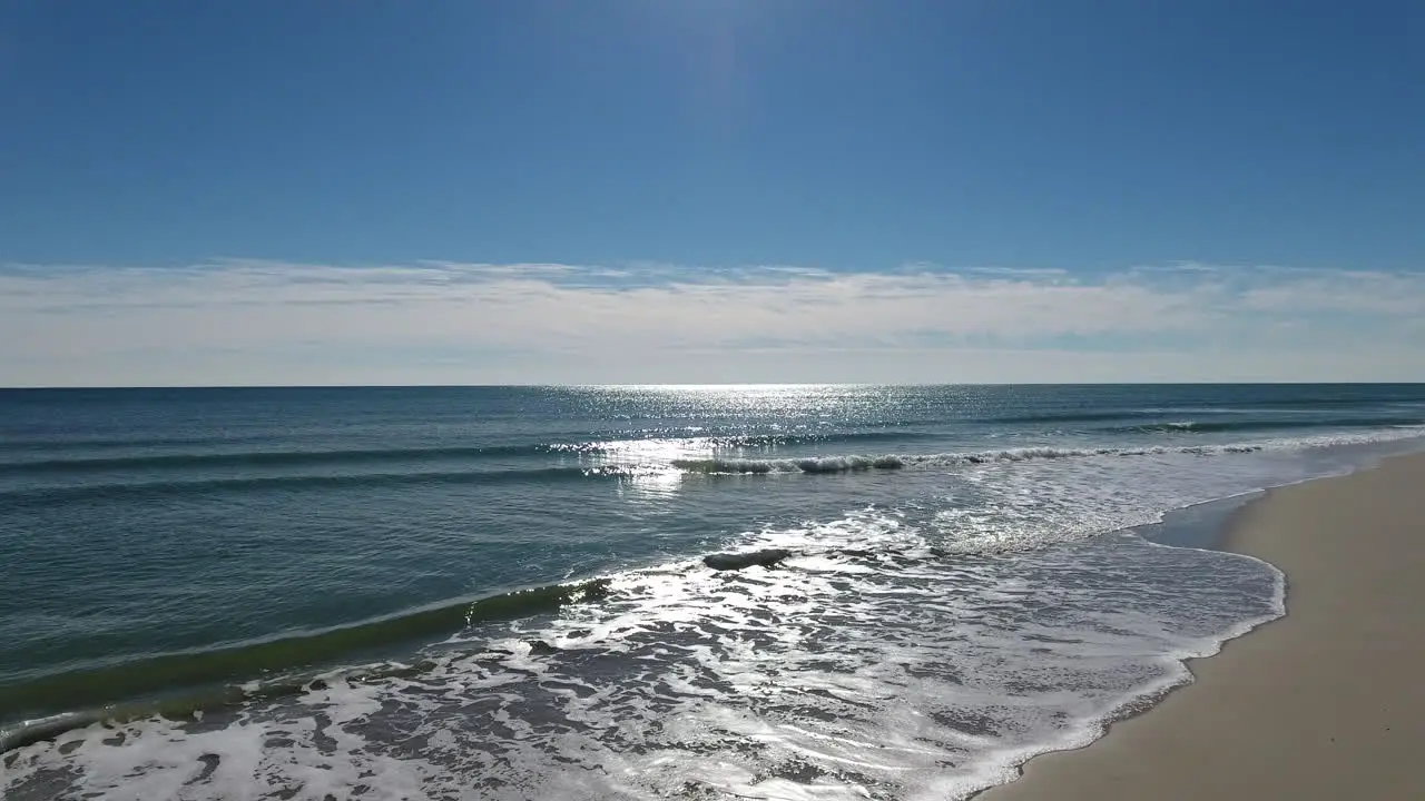 Drone shot flying towards gentle ocean waves crashing along the sandy beach