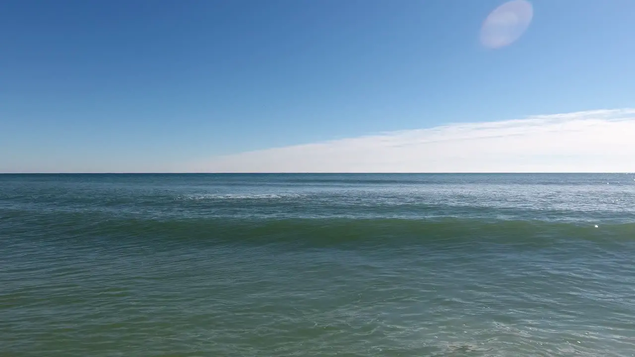 Tracking alongside an ocean wave on a calm blue sky afternoon