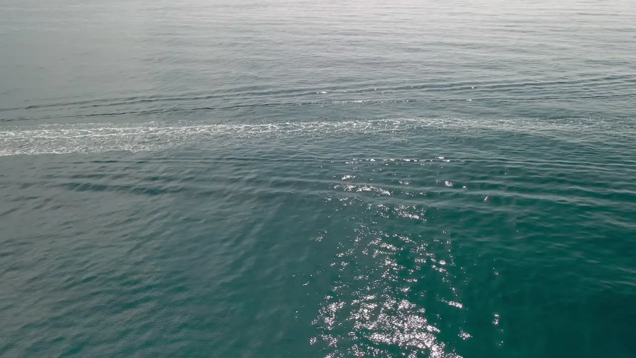 White trail and little waves from a boat passing over the Emeral Coast in Italy -aerial slowmo