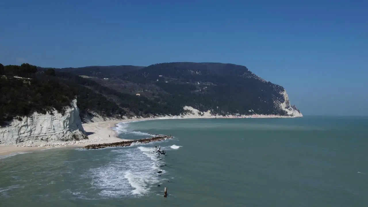 Sand beach with rocks cliffs green forrest hills and Adriatic sea waves clear sky early spring a couple walks on the beach