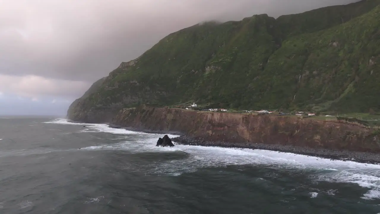 Fly towards rugged coastline with small town in Flores island Azores Drone shot