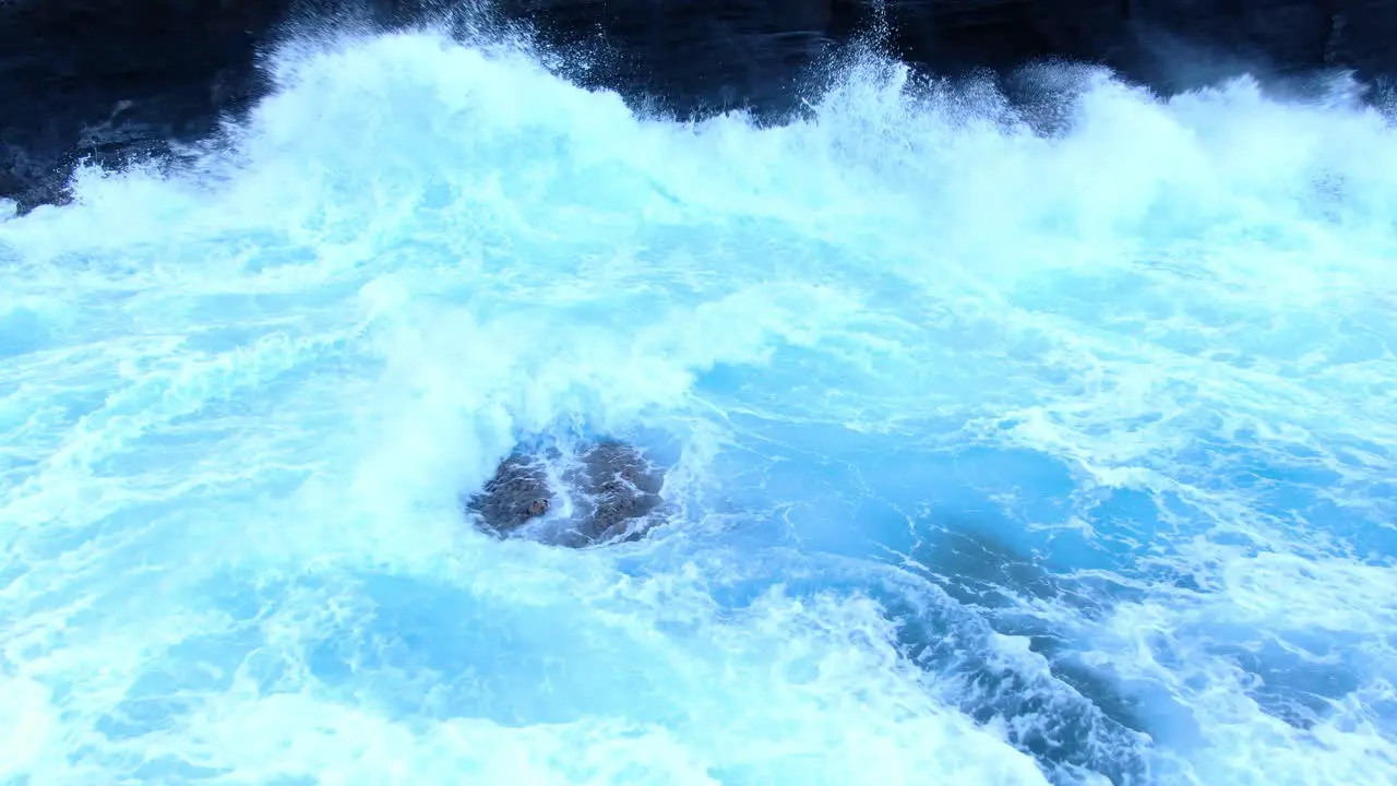 Drone close up of rough ocean wave white wash crashing against a cliff face