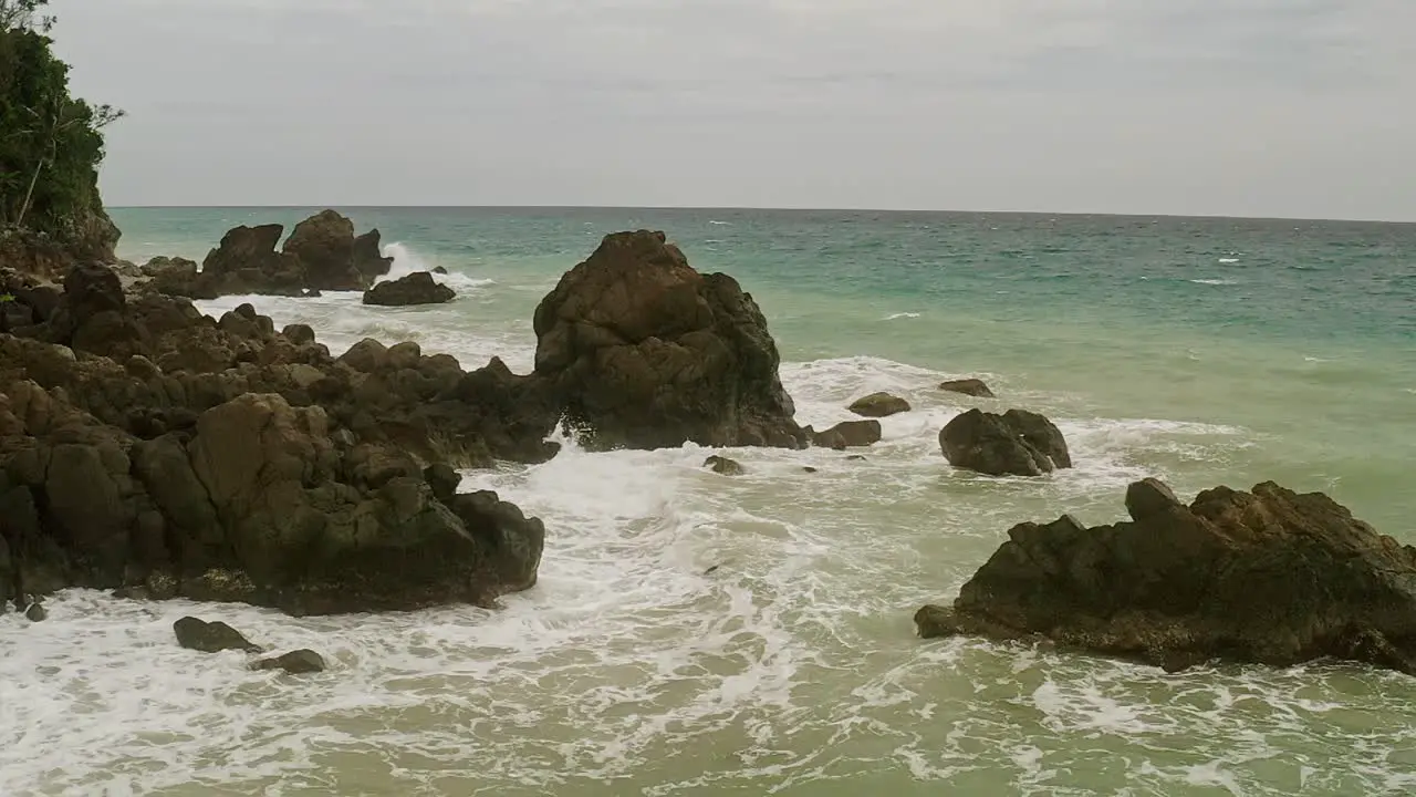 Aerial drone shot over waves crashing into the rocky coastline of Banbanon Beach Surigao Del Norte Philippines on a cloudy day