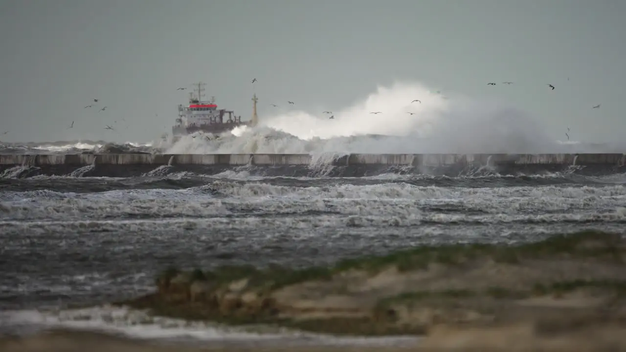 Wild coastal storm waves batter IJmuiden lighthouse and pier with ship in back