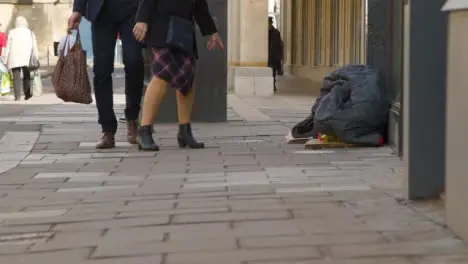 Wide Shot of Pedestrians Walking Past Homeless Persons Belongings On Street