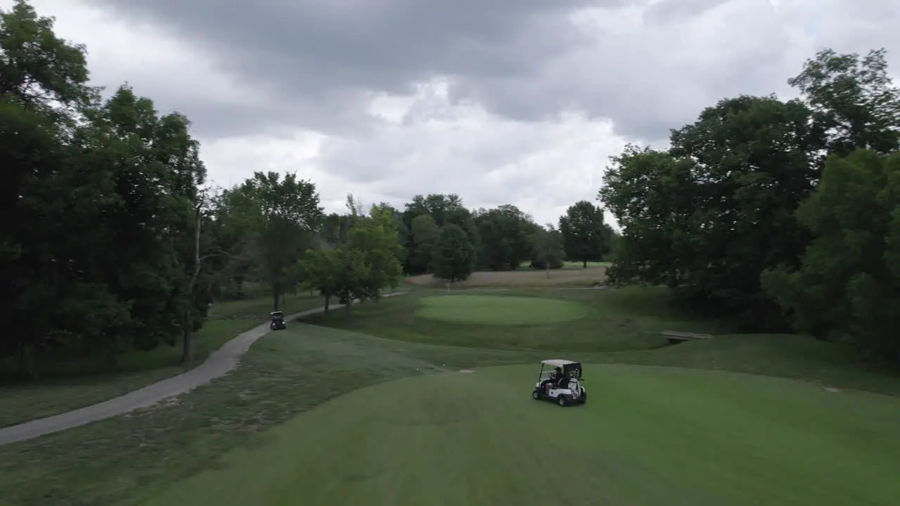 following golf carts driving on golf course aerial drone