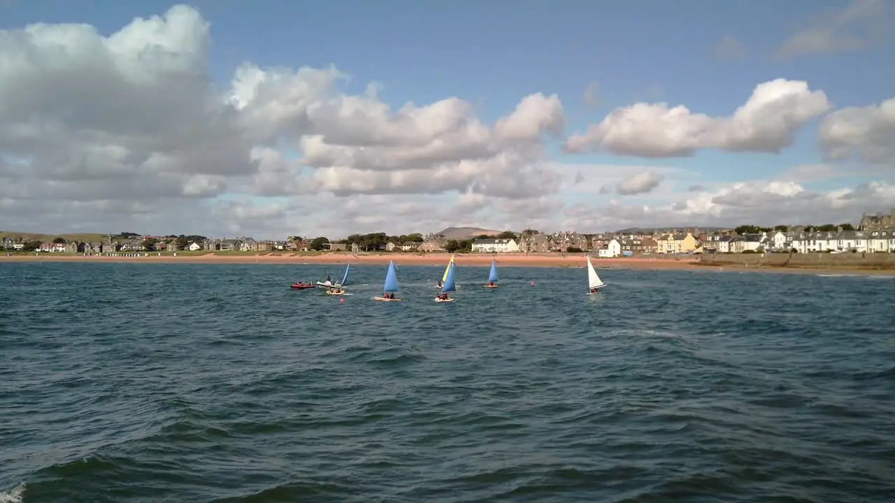 Young pupils being trained in small sailboats protected by motorboat overseers on choppy seas