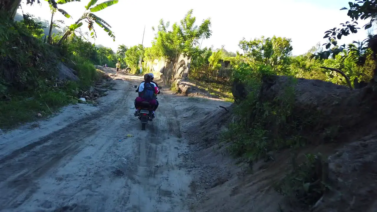 Footage of a running 2 wheeler motorcycle loaded with a passenger and baggage on a rough road