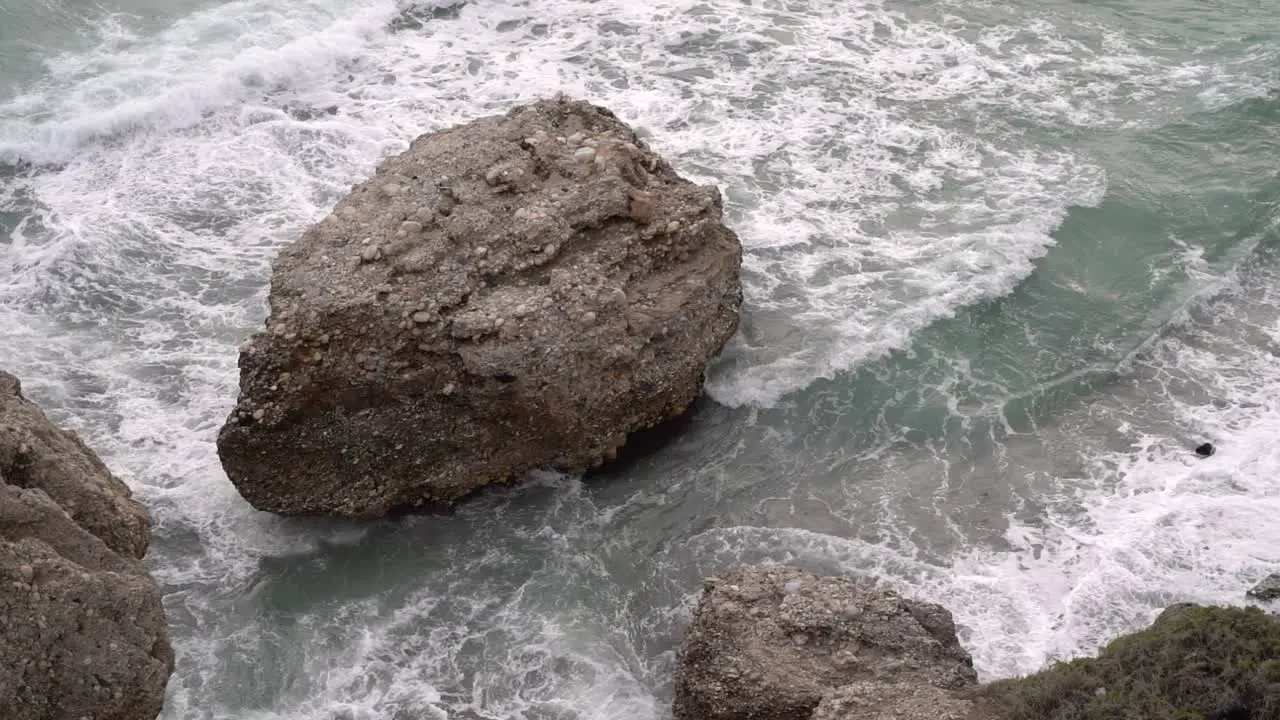 Big boulder in ocean withstanding waves in slow motion