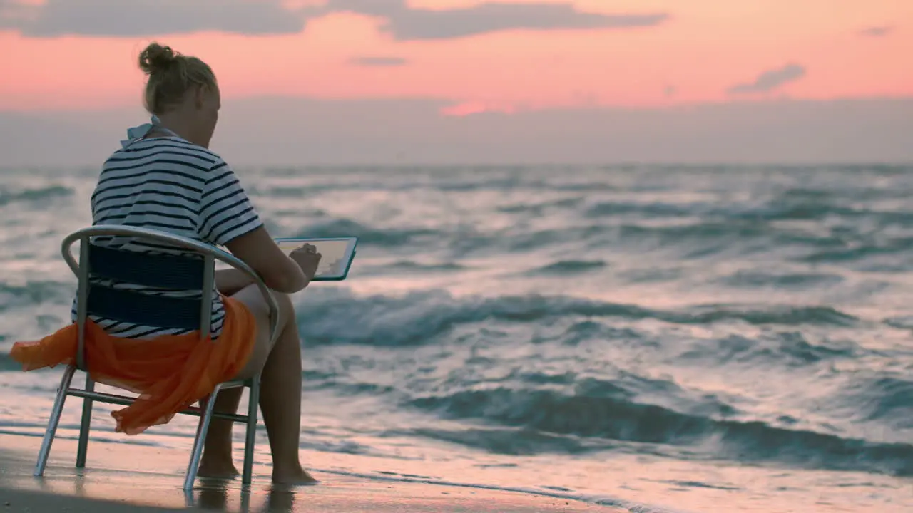 Woman with pad sitting on chair by rough sea