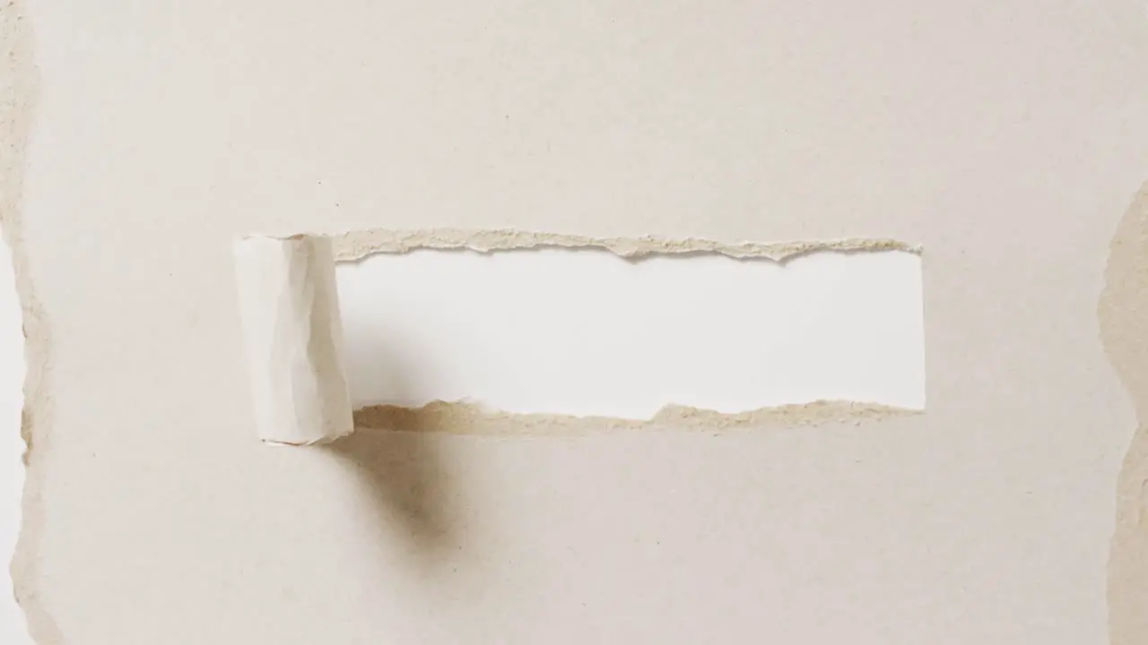 Video of close up of torn piece of beige paper on white background