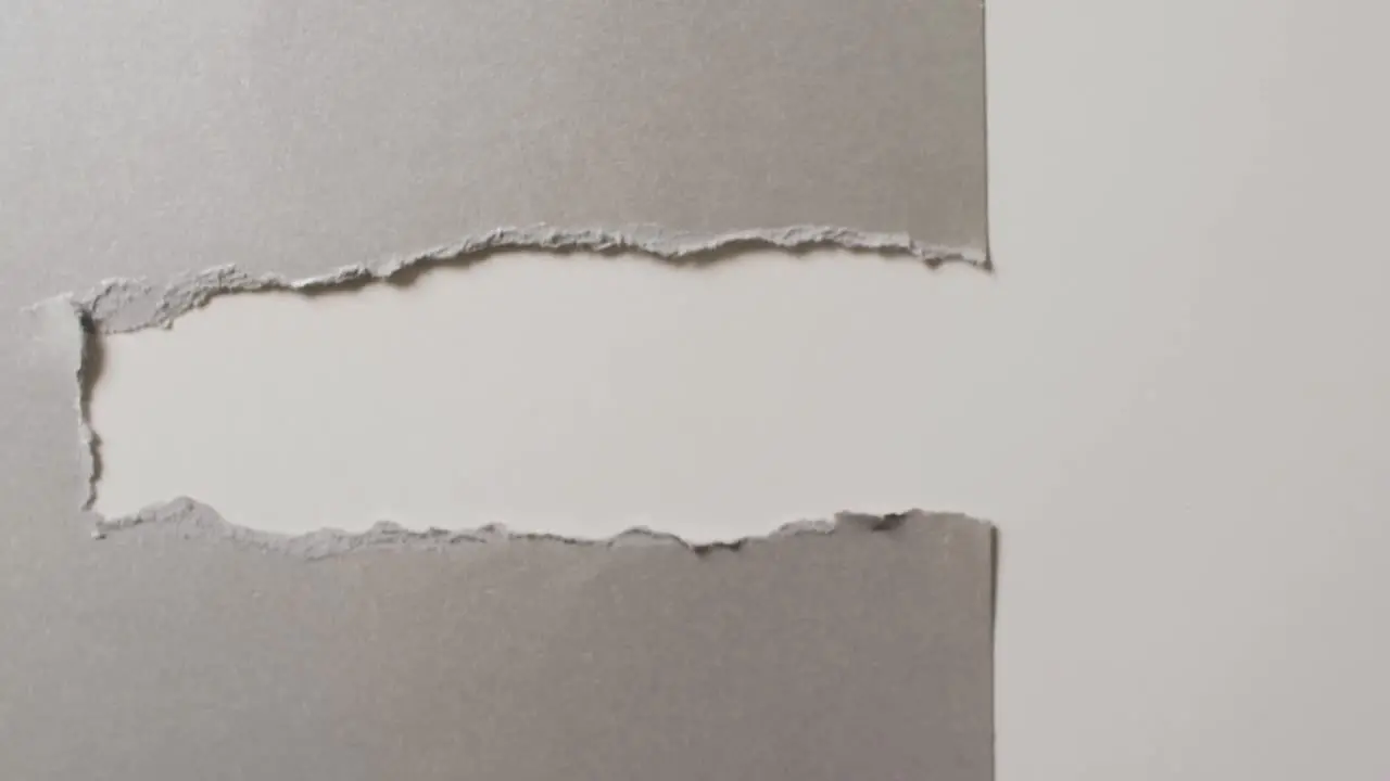 Video of close up of torn grey paper on white background