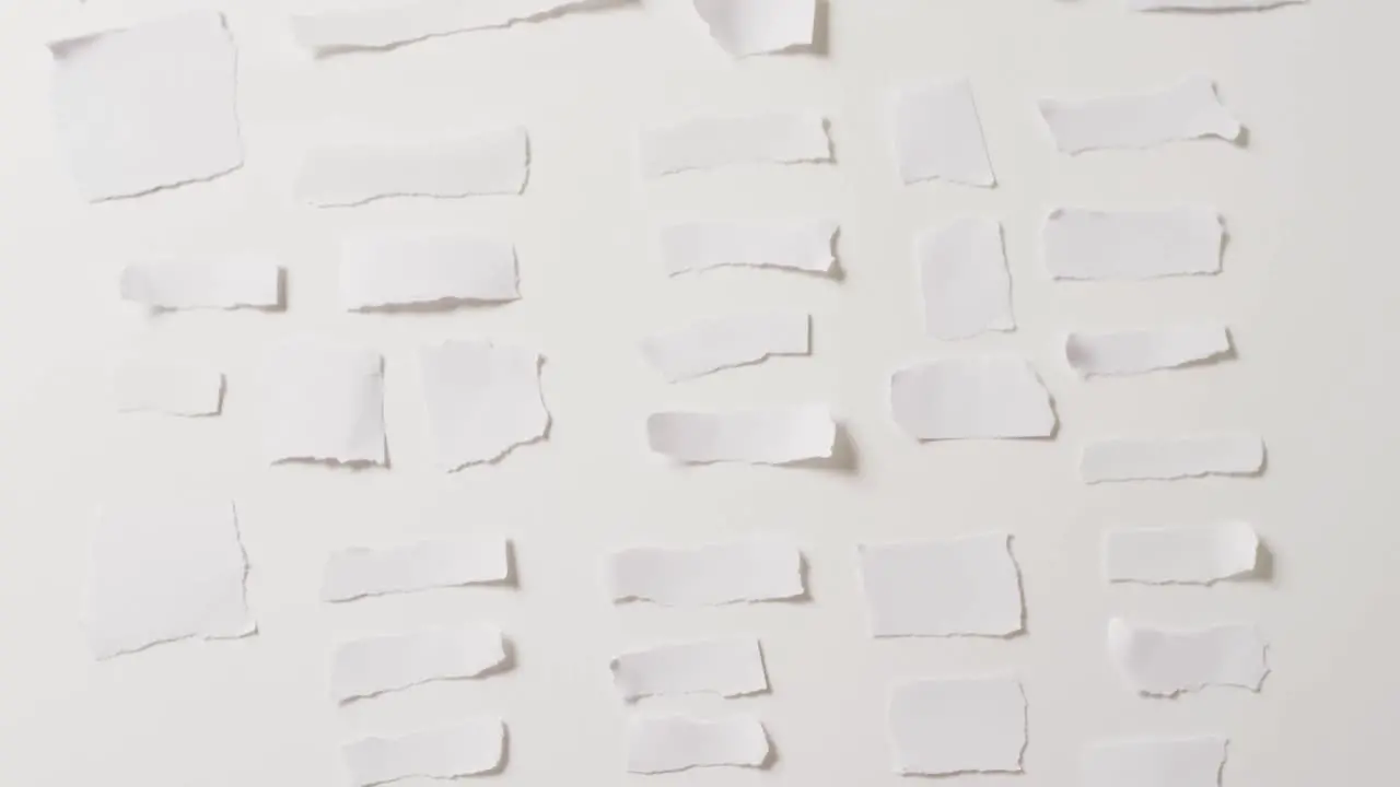 Video of close up of multiple torn pieces of paper on white background