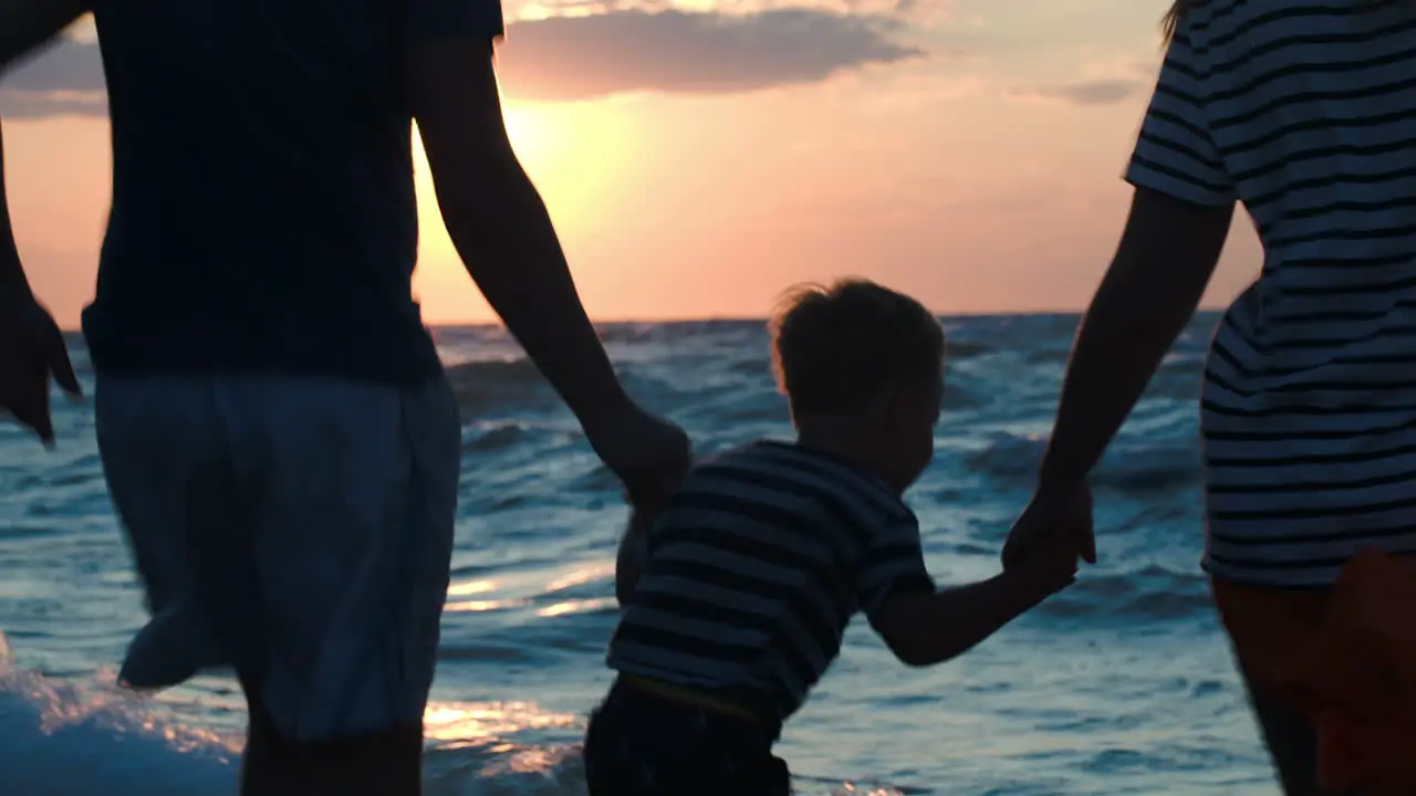 Happy family of three dancing by sea at sunset