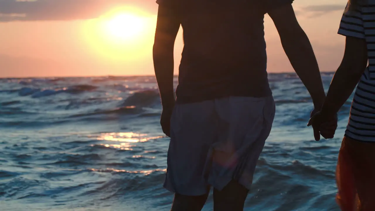 Loving couple holding hands by rough wavy sea at sunset