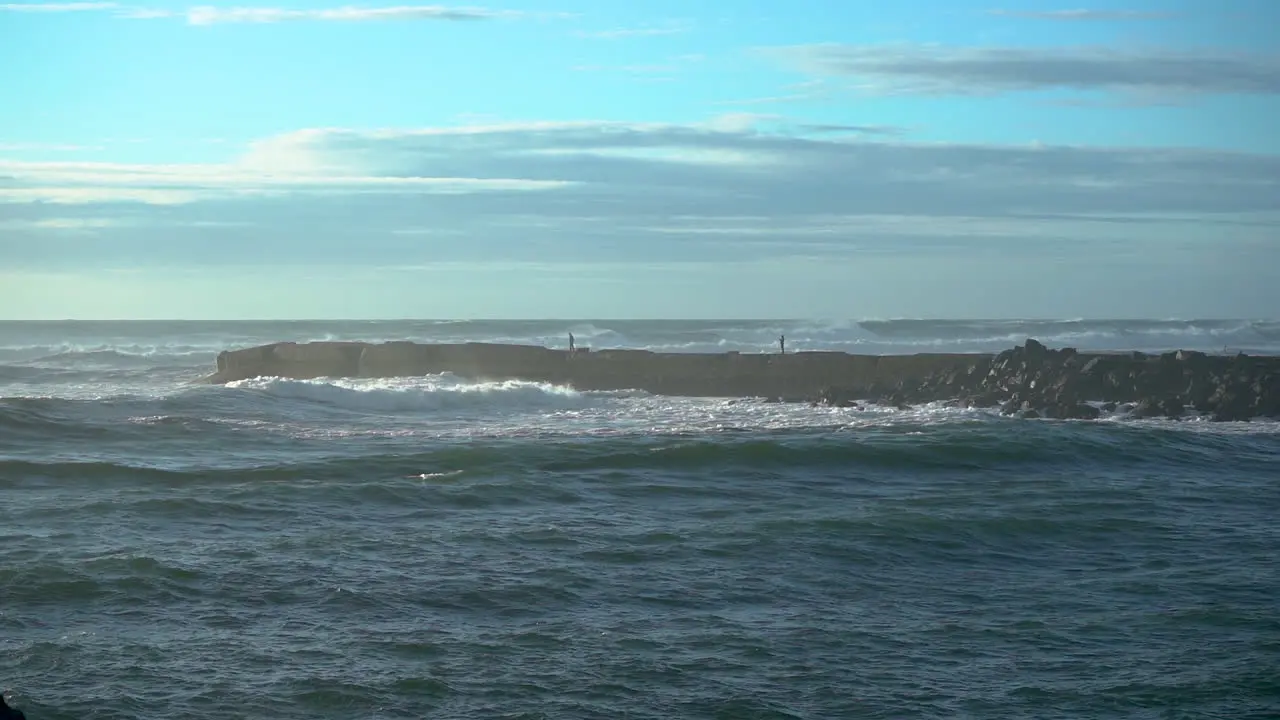 Two foolish people on a jetty in Bandon Oregon during strong wind and waves ignorant about the dangers