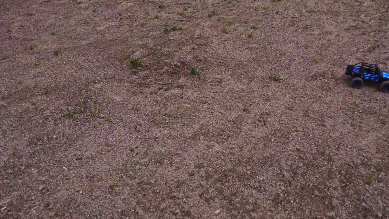 A small model RC truck competes in a hobby race driving over rough terrain with an aerial view from a drone