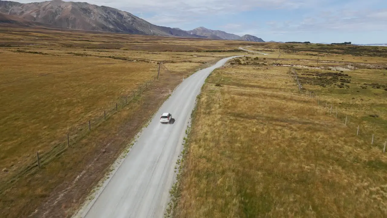 White SUV on dusty gravel road in rural countryside with mountains in background