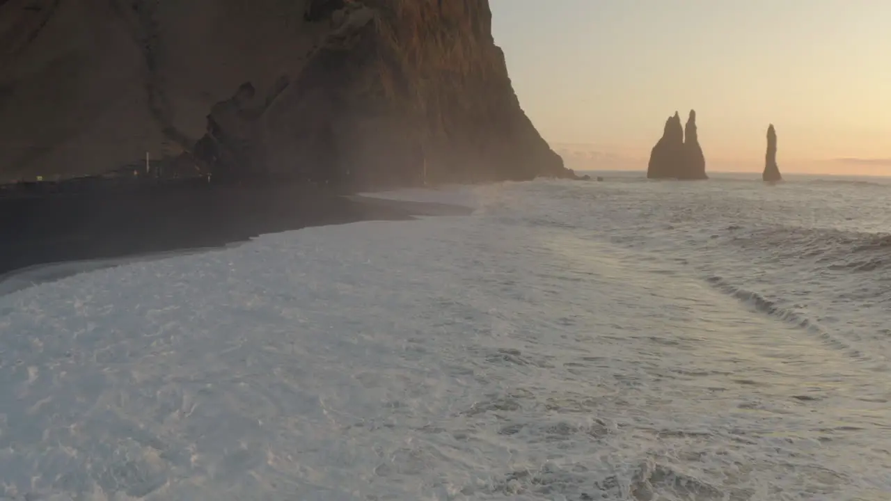 Slow aerial shot over black sand beach towards Columnes Reynisfjara and sea stacks Iceland