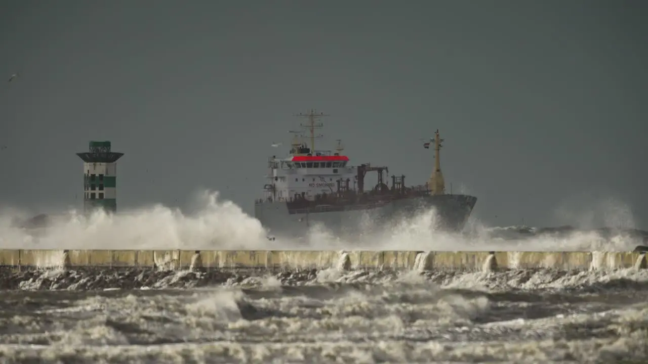 Storm waves crash over cement IJmuiden pier with ship in background telephoto