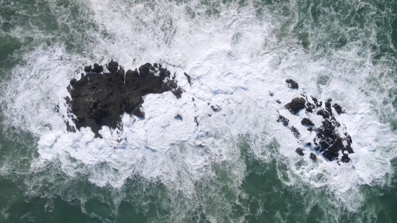 Powerful ocean waves pounding on rocky island aerial top down view