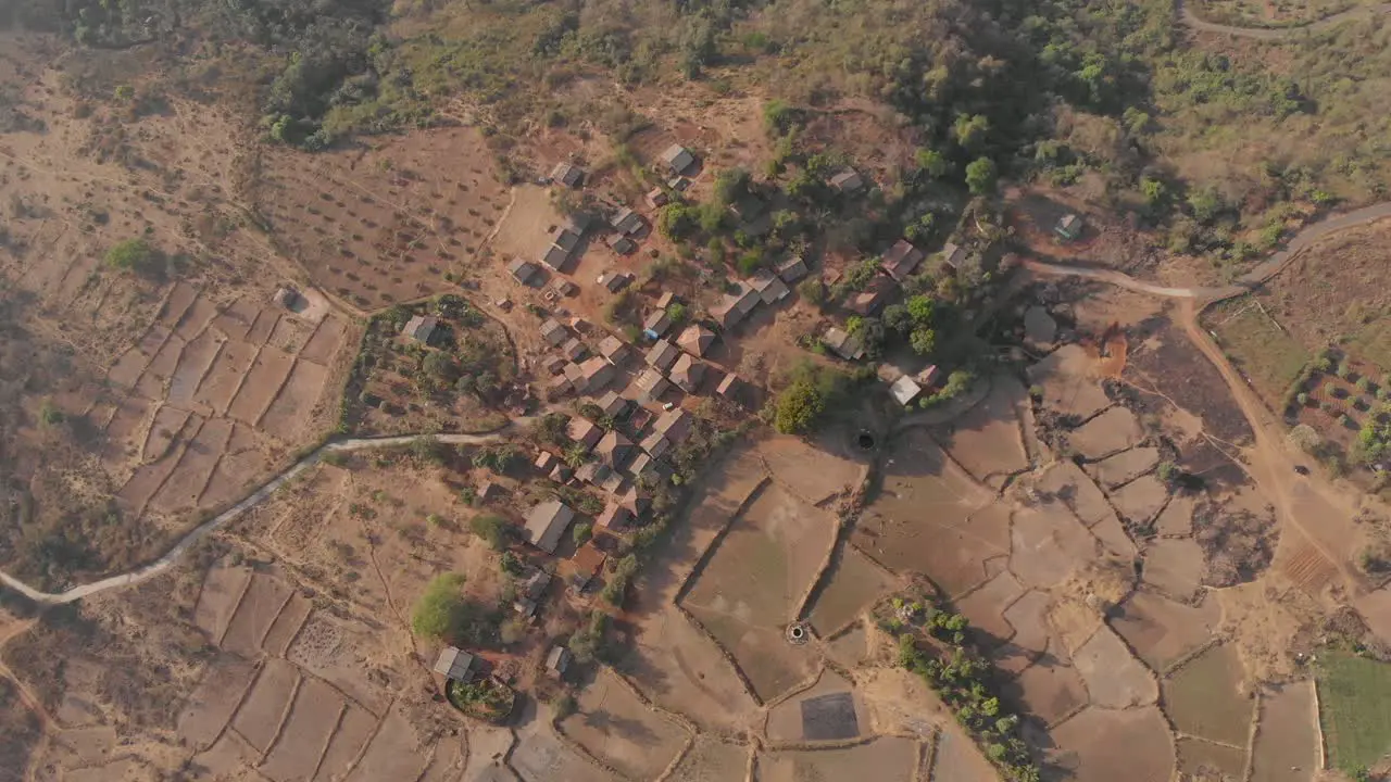 Falling drone shot of a rural Indian village surrounded by farmlands