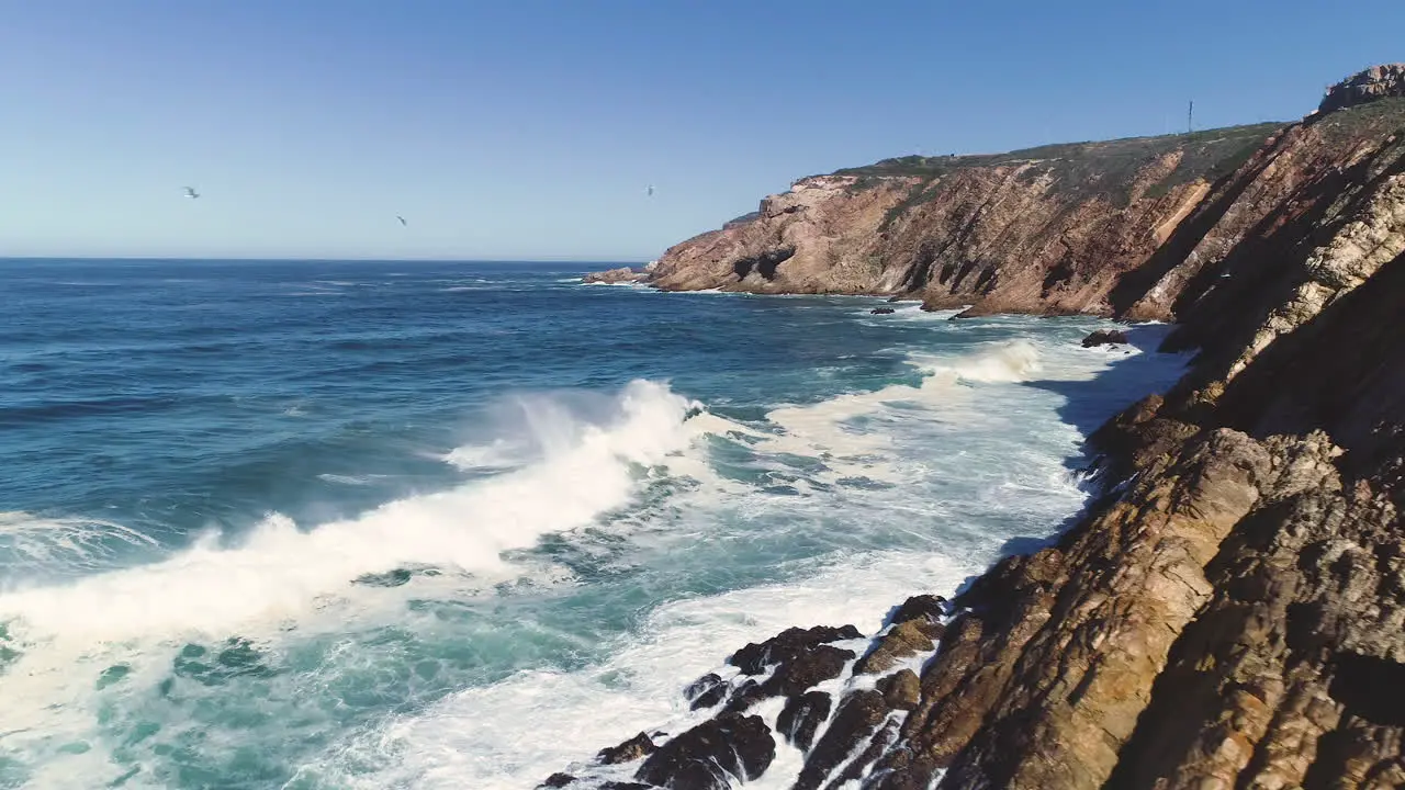 Aerial Flying from rocky coastline over heavy waves crashing into sheer cliffs The Point Mossel Bay