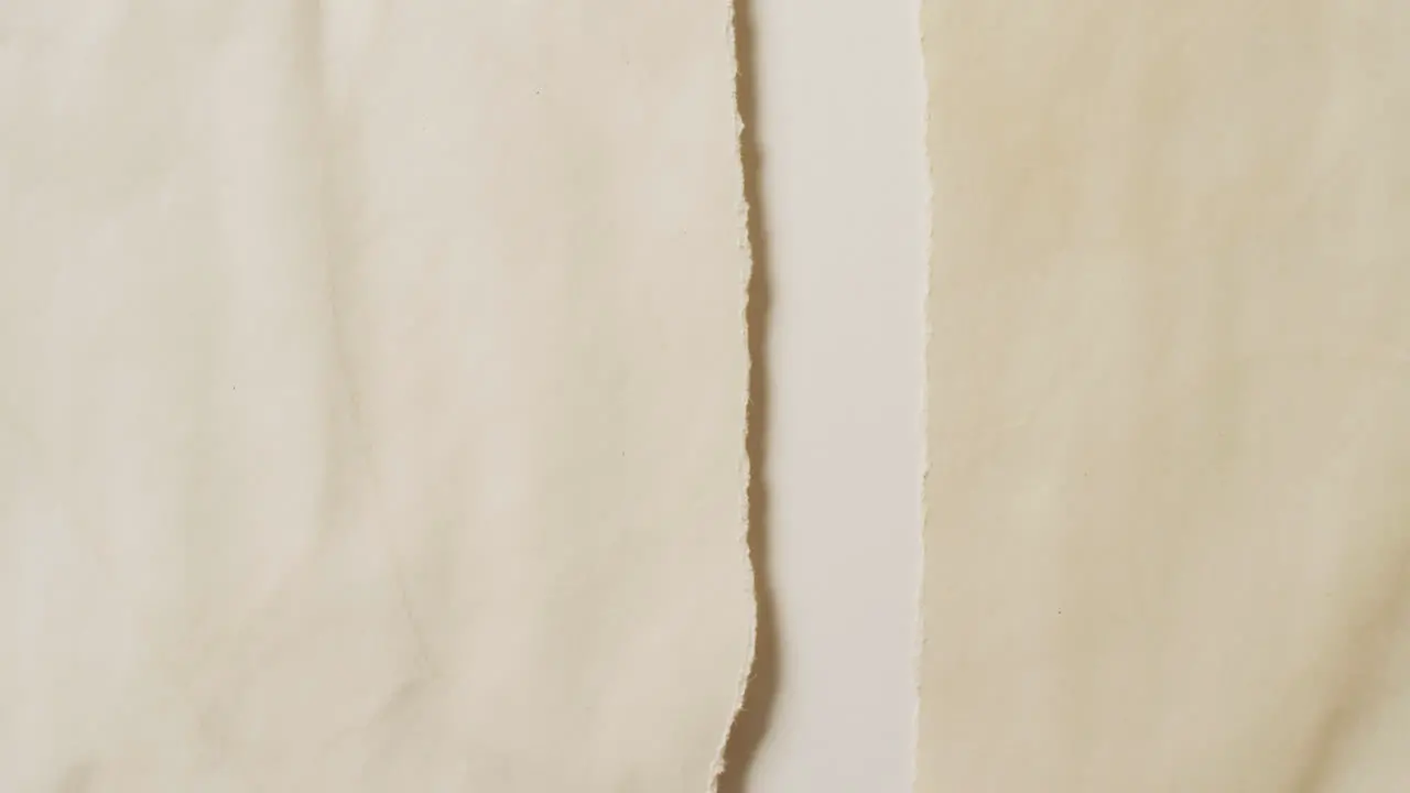 Video of close up of torn pieces cream paper on white background