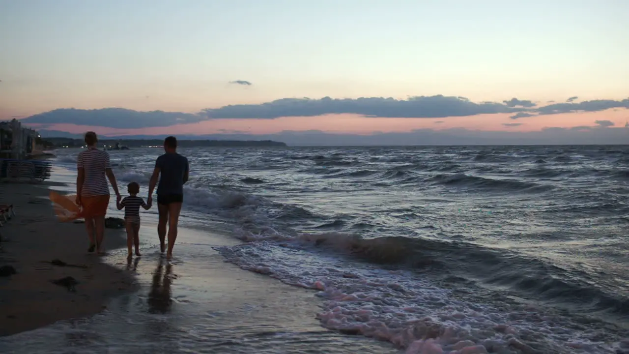 Family of three walking barefoot along the shore