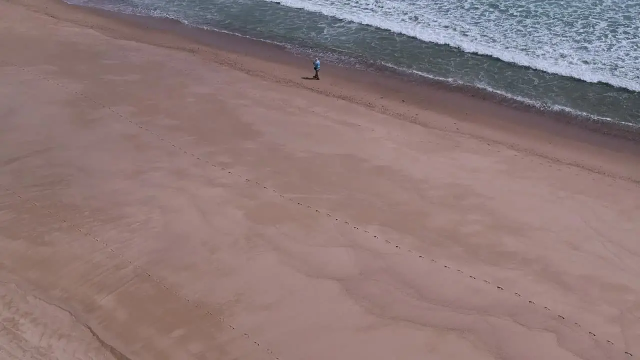 Slow Drone Fly Over Male Fisherman Walking Alone Beach Shoreline Waves Crashing