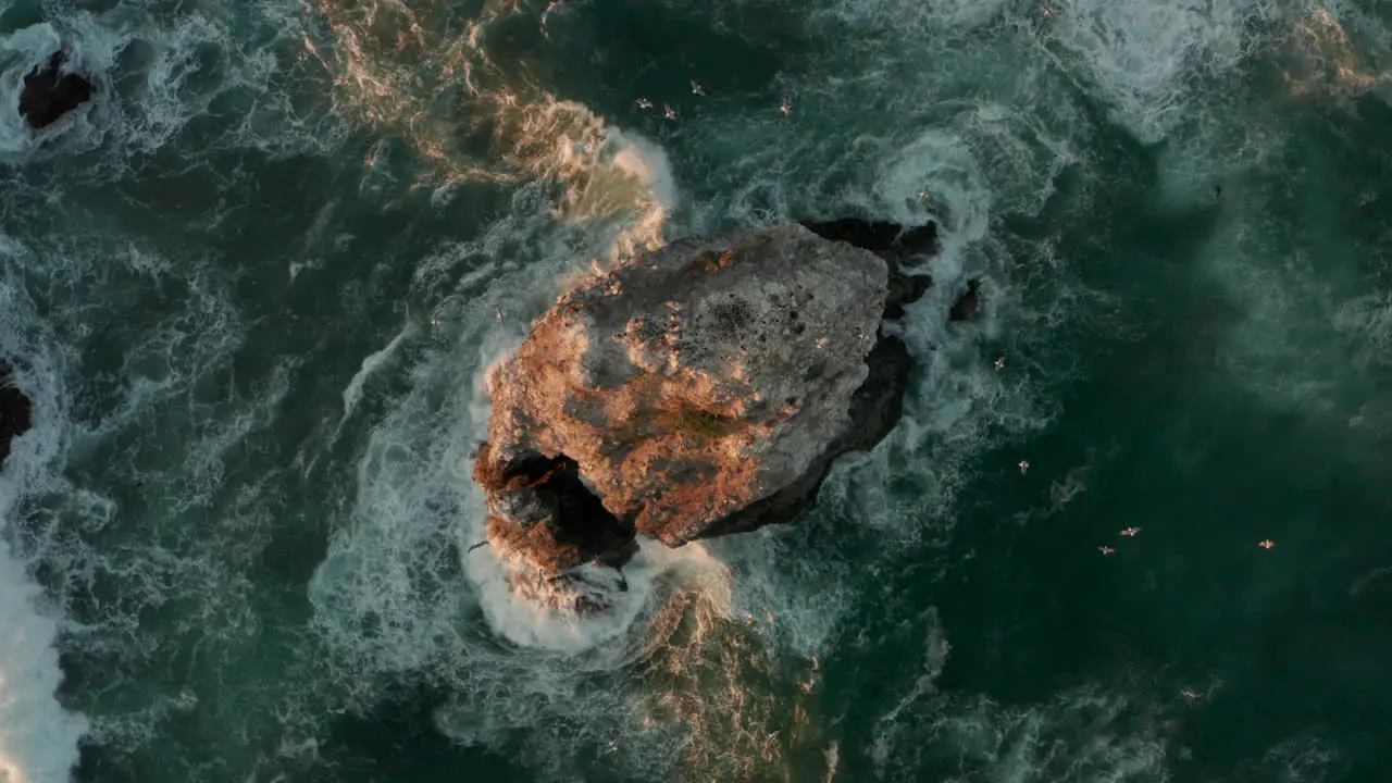 Top down aerial shot of waves crashing against a sea stack