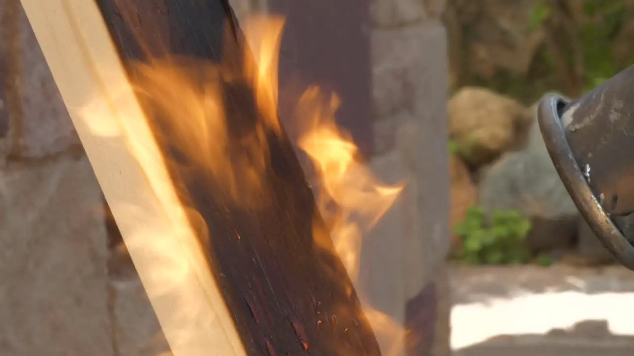 Propane blowtorch burning pine wood plank with strong flame closeup