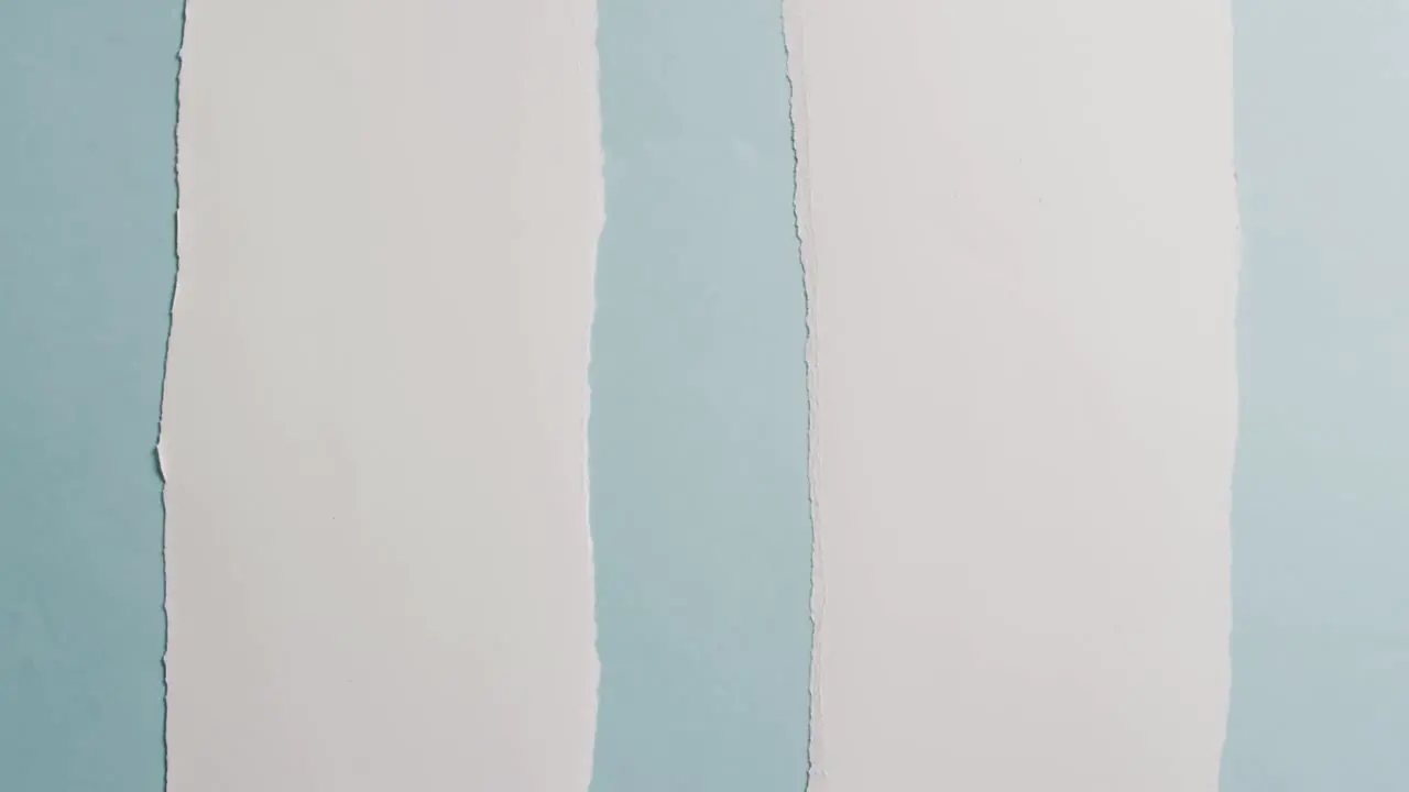 Video of close up of torn pieces of white paper on blue background