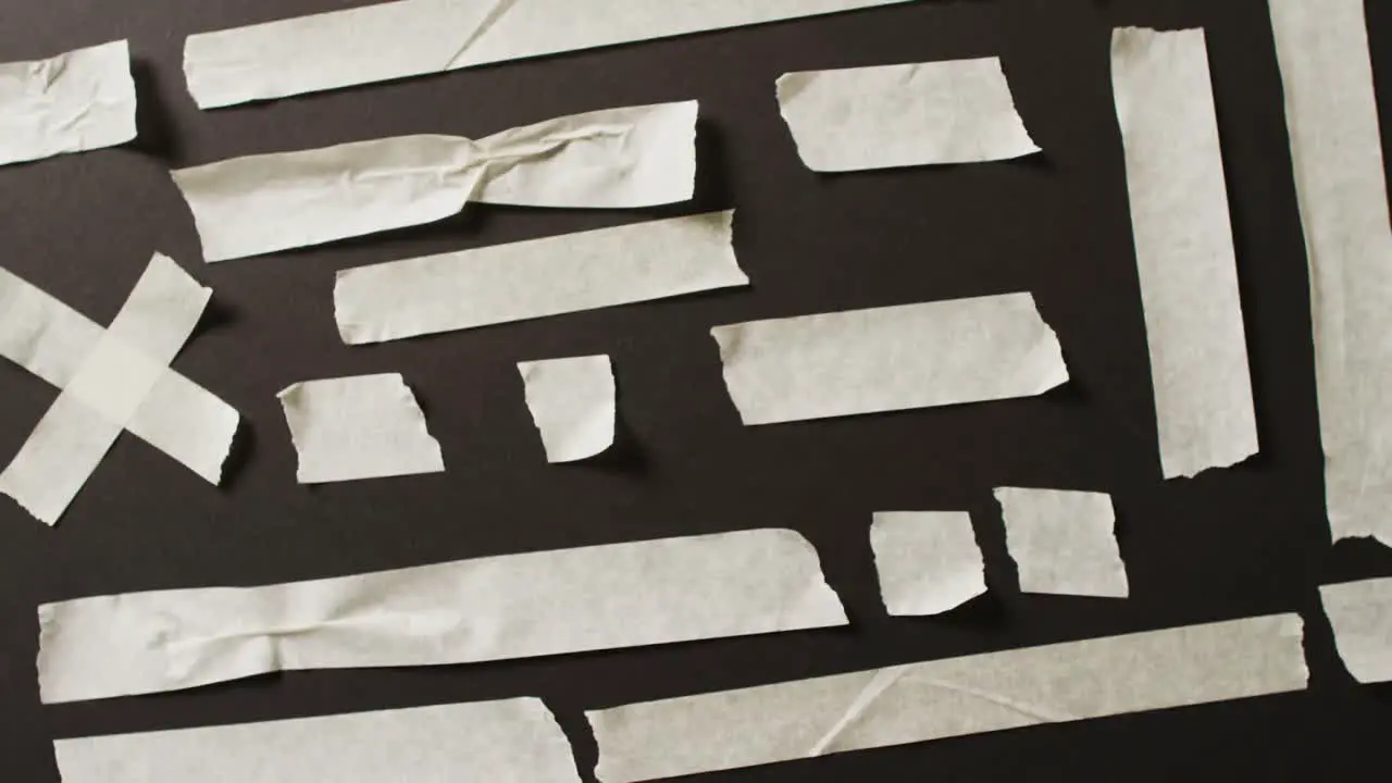 Video of close up of multiple white paper tape pieces on black background