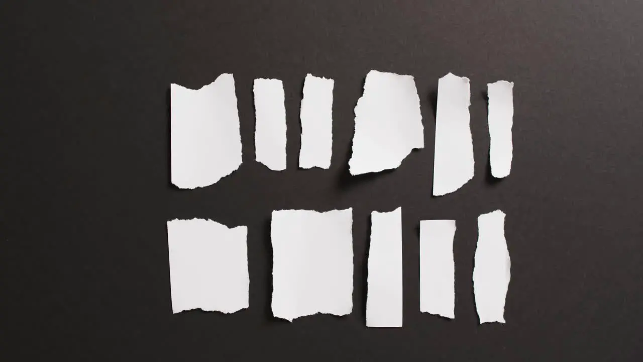 Video of close up of multiple torn piece of white paper on black background