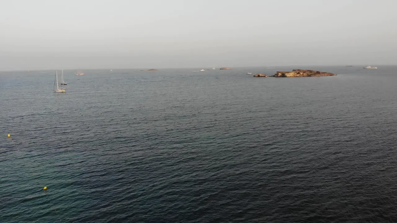 Relaxing aerial view of two sailing boats and a small balearic island in Mediterranean sea with calm waves on warm summer afternoon sunset in Eivissa Ibiza Spain