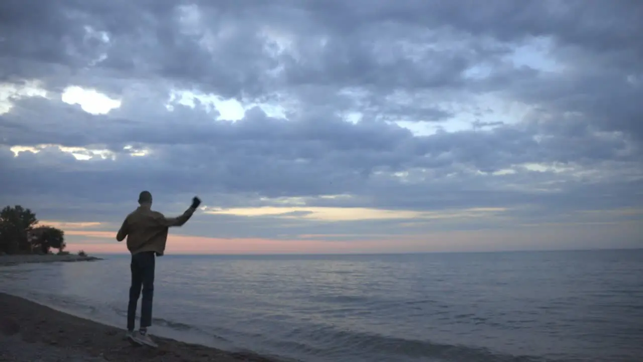 Man Happily Jumps And Stretches By The Beach Overlooking A Wonderful Pink And Purple Sunset wide shot