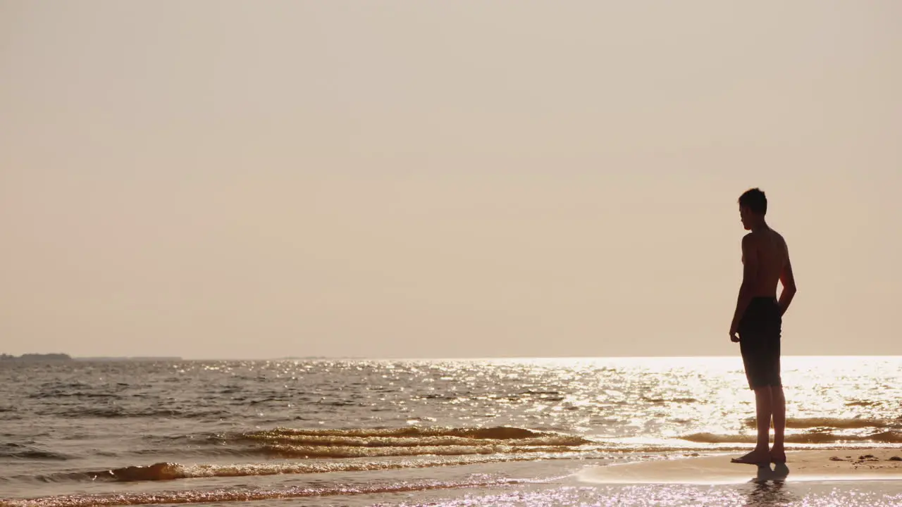 Silhouette Of A Young Single Man Standing On A Small Island Of Sand Looking At The Glare Of The Sun 