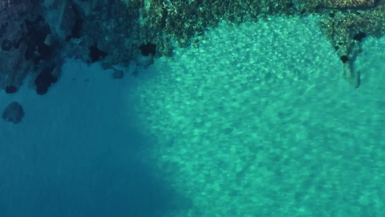 Backward aerial of rugged coastline down to to turquoise clear water tilt down