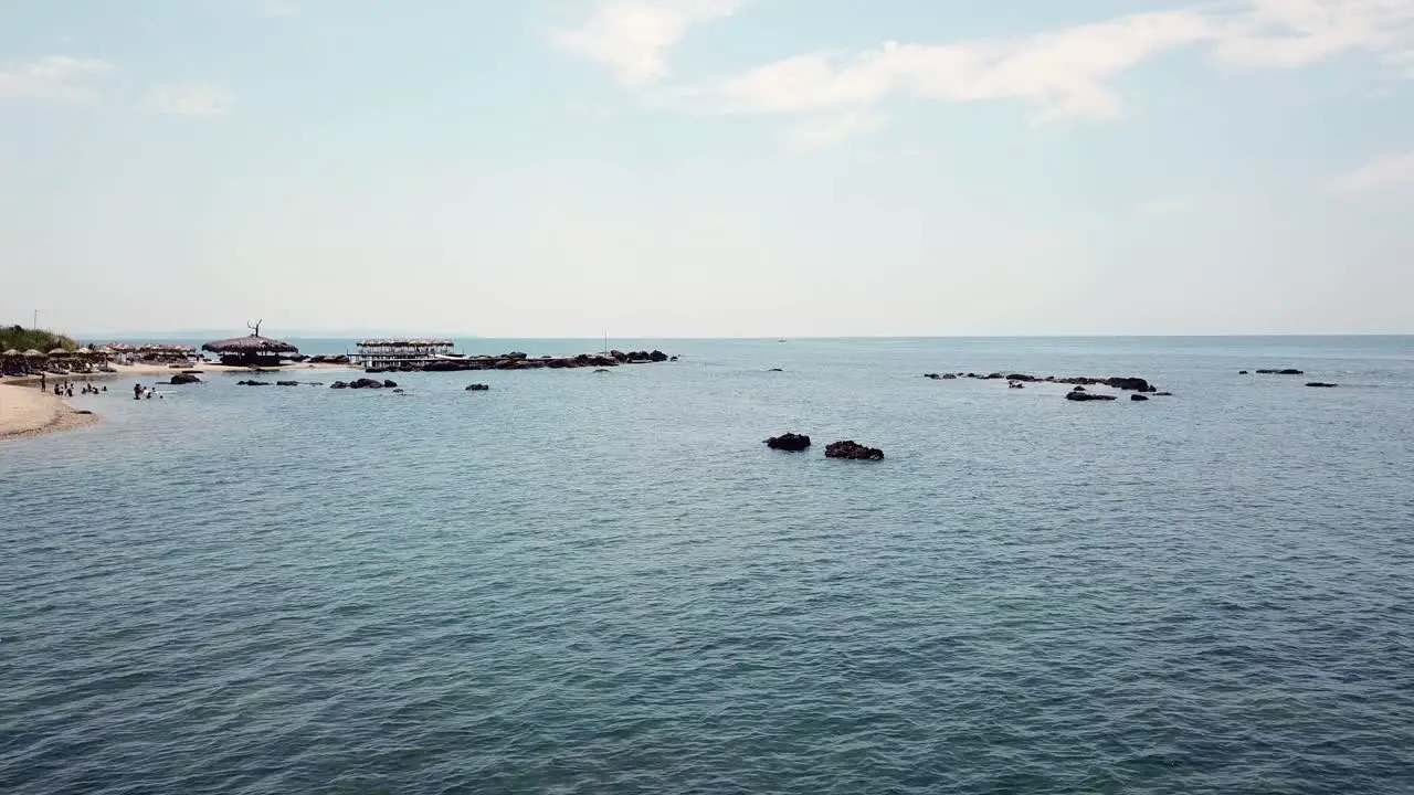 Small rocky beach with umbrellas and people going swimming in the sea