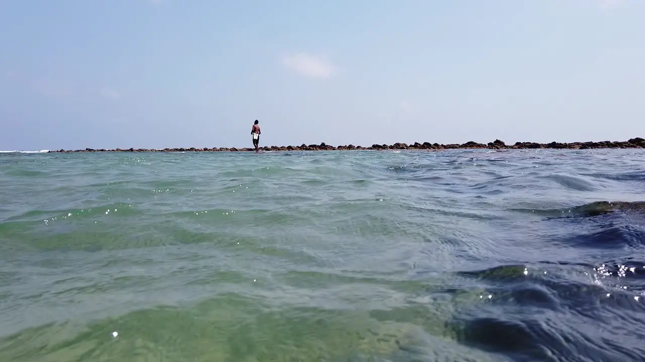 Fisherman casting a hook on a line whilst standing on the coral reefs at high tide with a wind blowing across the andaman sea towards the shore