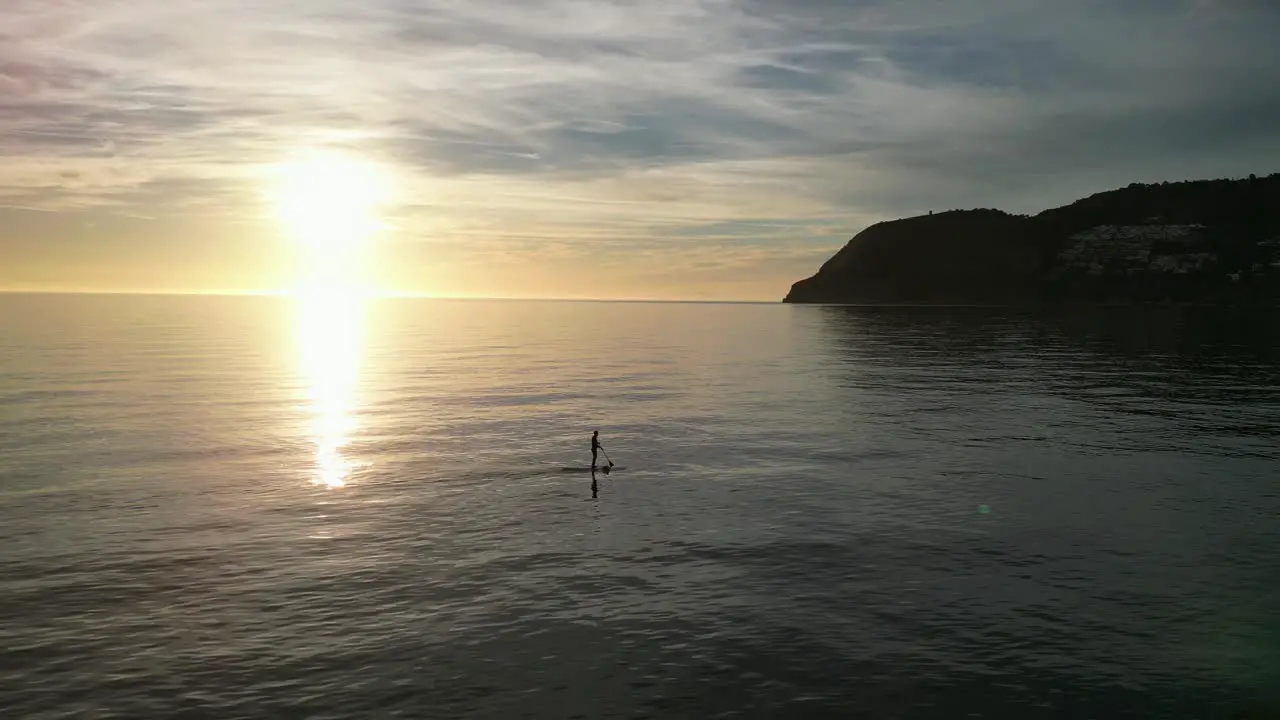 Silhouette of adult man stand on SUP board paddle during sunset in Spain