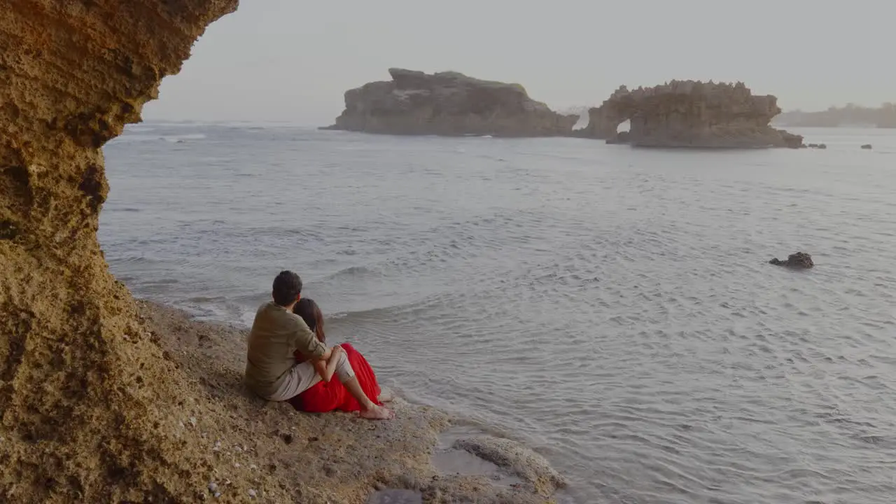 Couple Sitting On Beach Enjoying Beautiful Seascape Rocks Formation In Water