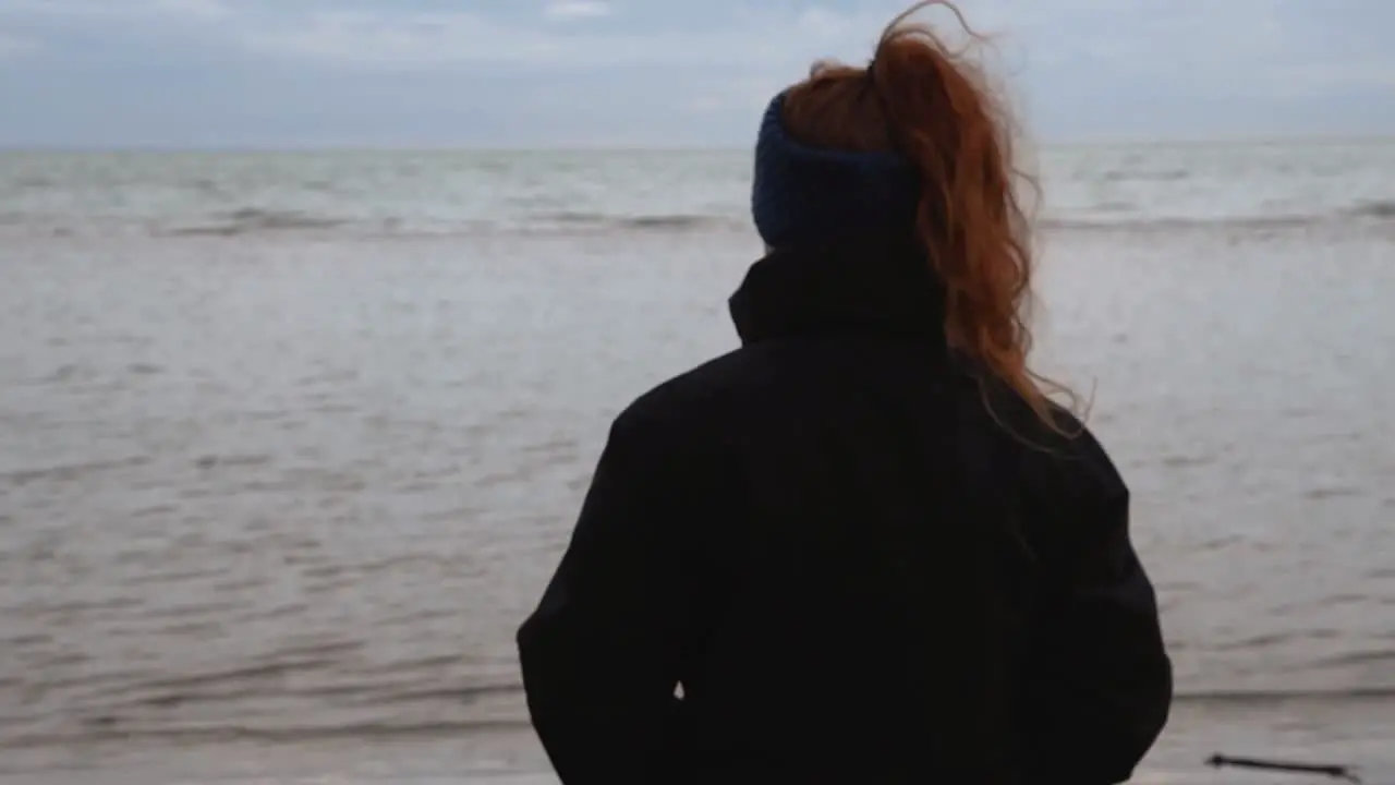 sad and melancholy beach and sea landscape with a girl with beautiful red hair watching it in a cold and windy winter day