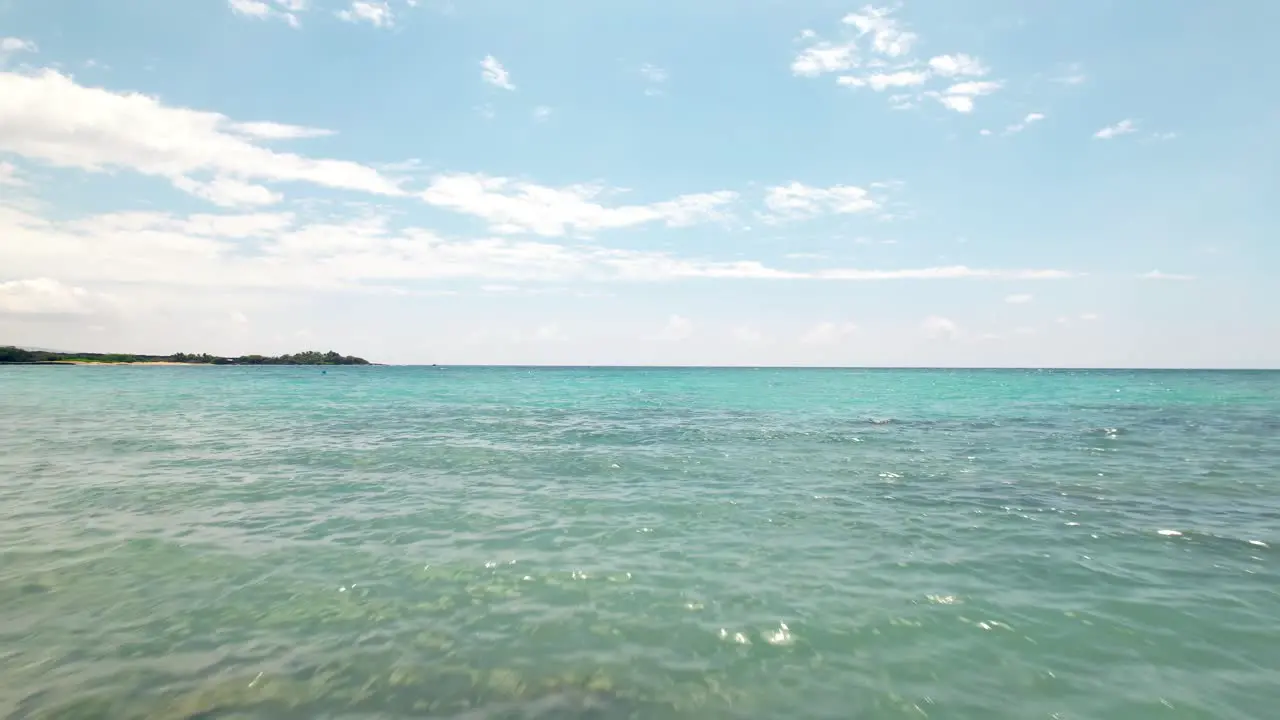 Low altitude aerial fast flight along a beach and a lounge chair then over the turquoise ocean water towards the distant horizon