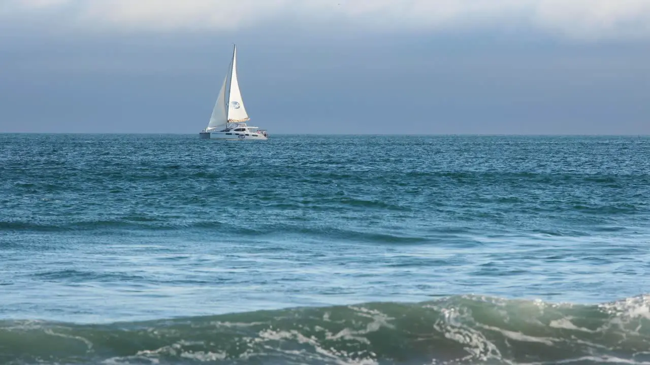 side view of Catamaran sailboat sailing in full sail on a dark blue sea with reflections in backlight