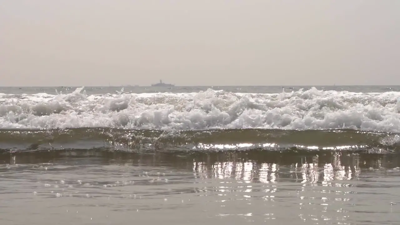 Close up of Pacific ocean waves crashing down onto the sandy beach San Diego California with a large ship in the background