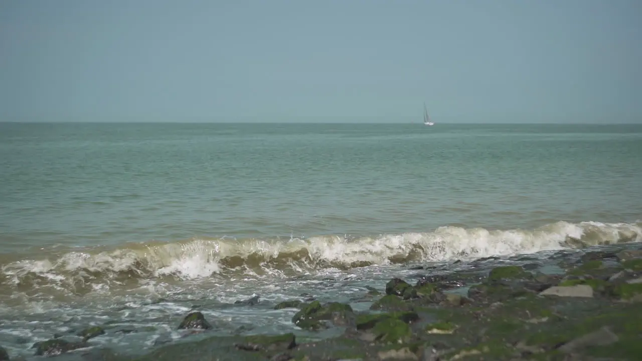 Waves on the coast with a sailing ship in the background slow motion